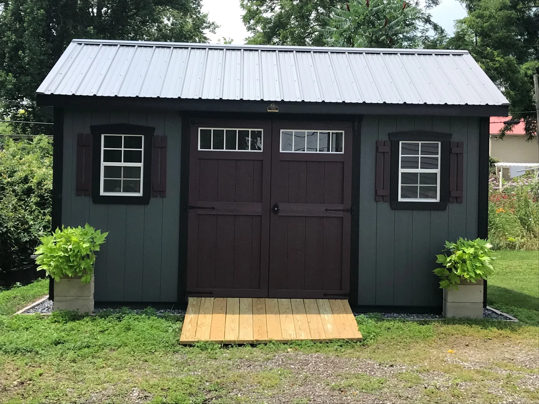 Custom backyard shed, dark exterior and dark doors with a grey roof and walkway.