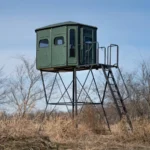 Redneck elevated hunting blind with dark green exterior located on a field.