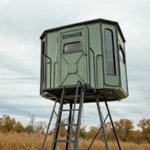 Redneck elevated hunting blind with dark green exterior located on a field.