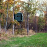 Redneck elevated hunting blind with dark green exterior located on a field.
