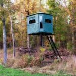 Redneck elevated hunting blind with dark green exterior located on a field.