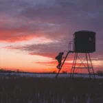 Redneck elevated hunting blind with sunset in the background in a field.