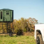Dark green Redneck elevated hunting blind on trailer in hunting field.