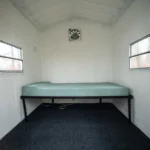 Redneck hunting cabin interior with bed, windows, and fan.