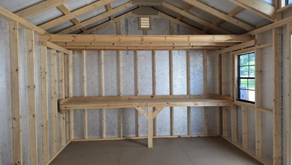 Shed interior with a wooden workbench, wall shelves and windows.